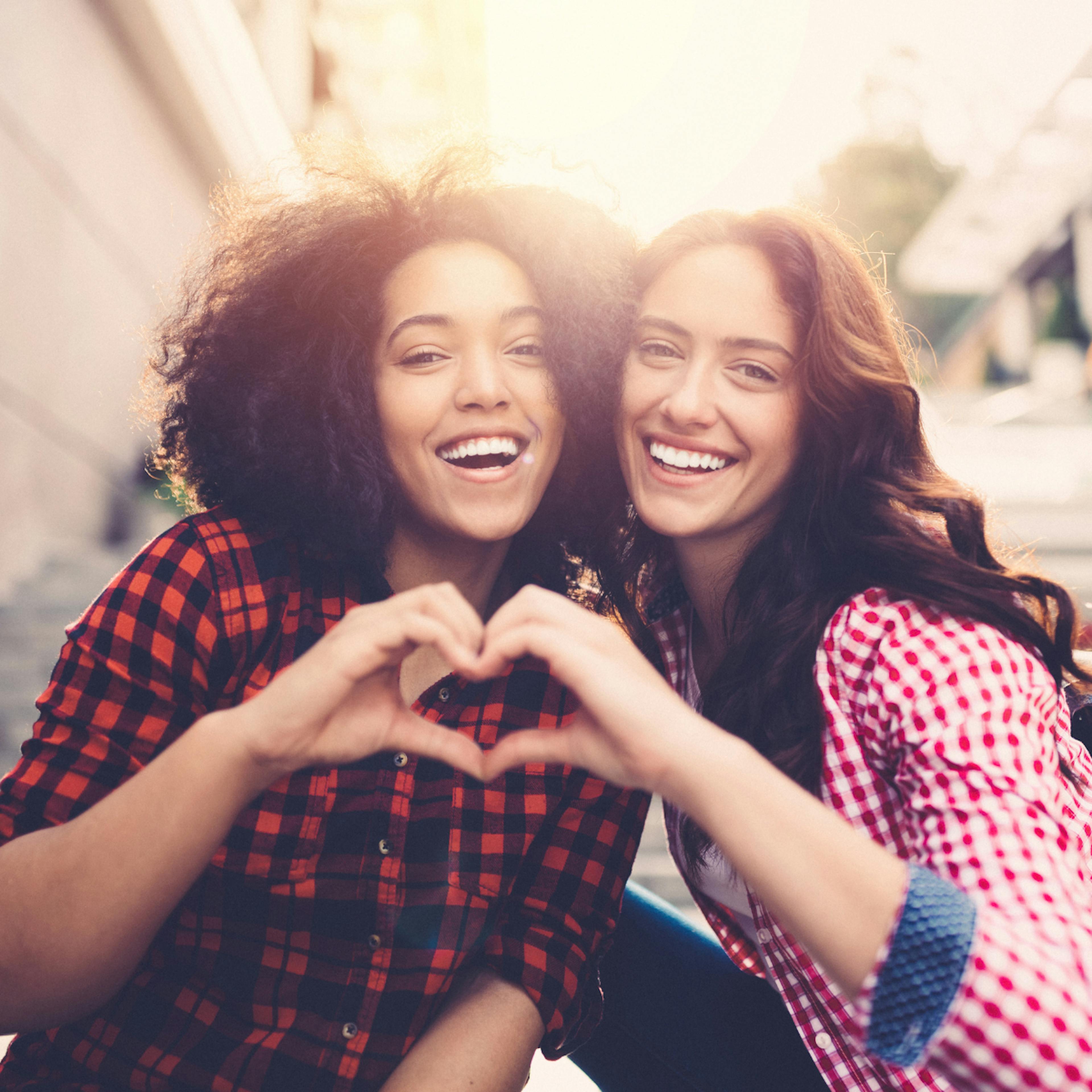 image of two friends smiling and forming their hands into a heart shape together symbolizing friendship 