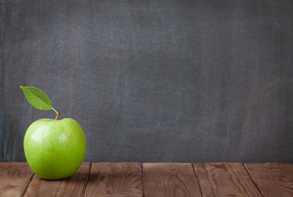 Green Apple sitting on table in front of blackboard