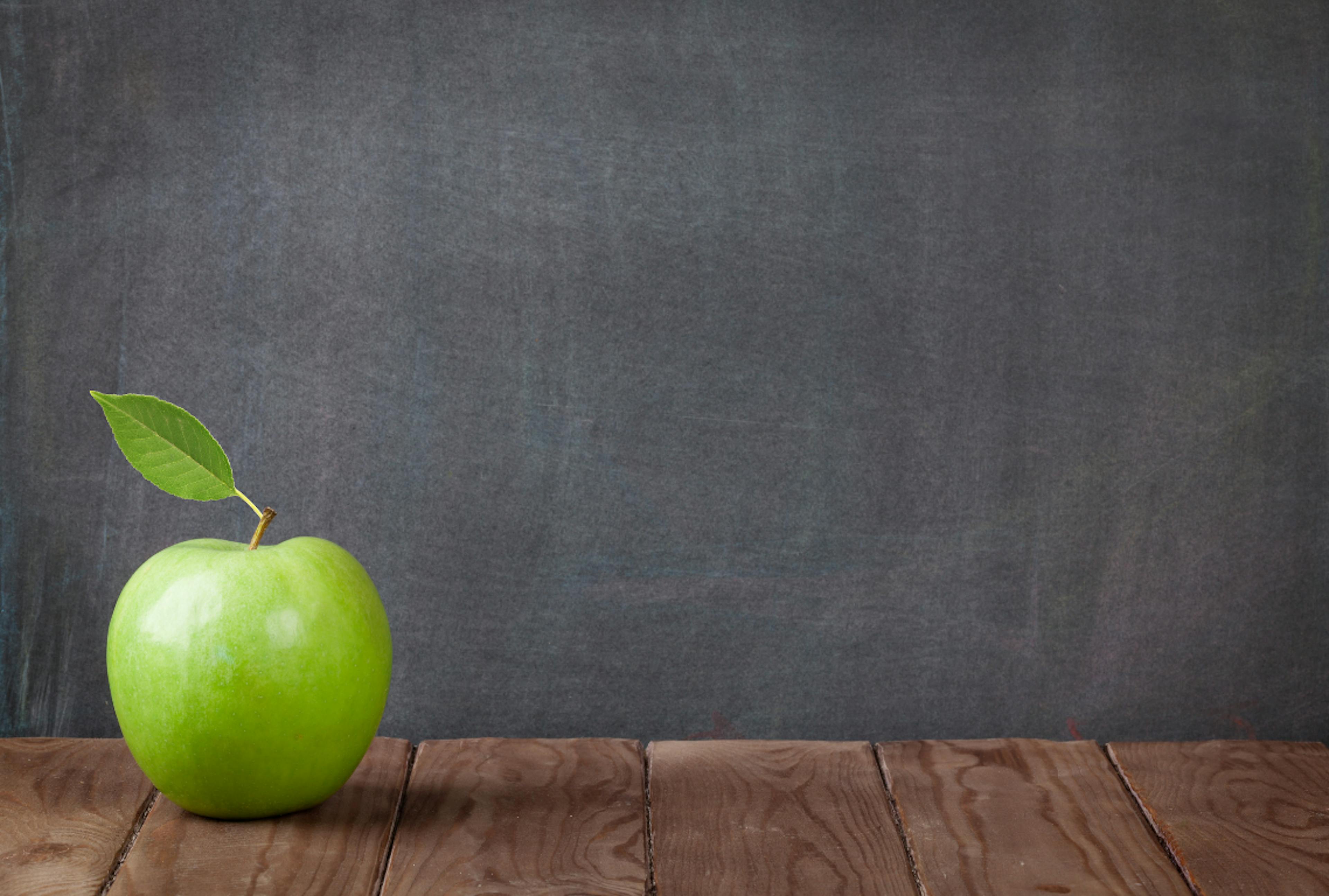 Green Apple sitting on table in front of blackboard 