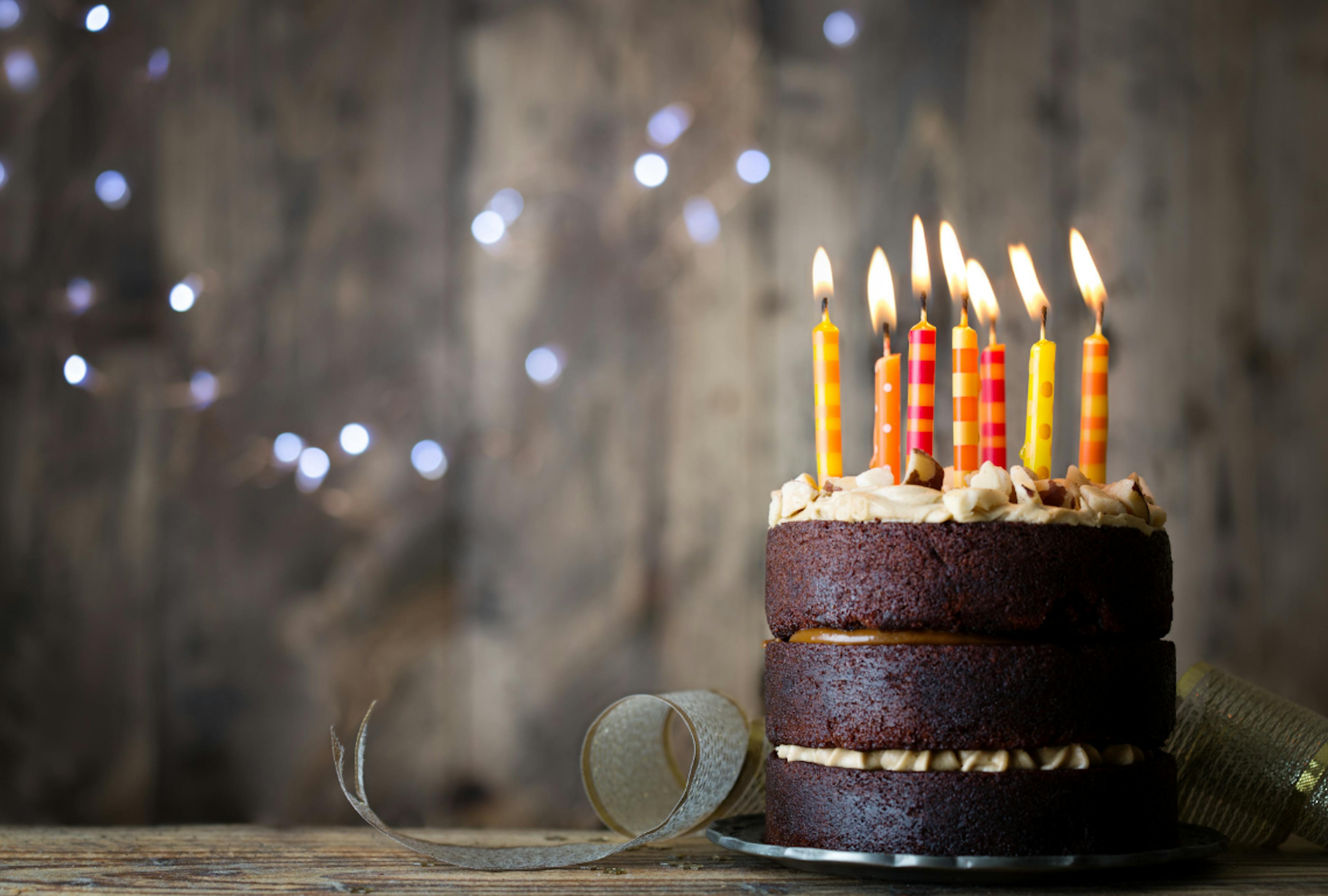 Chocolate layered Birthday cake with colourful lit candles and a whimsical brown background 