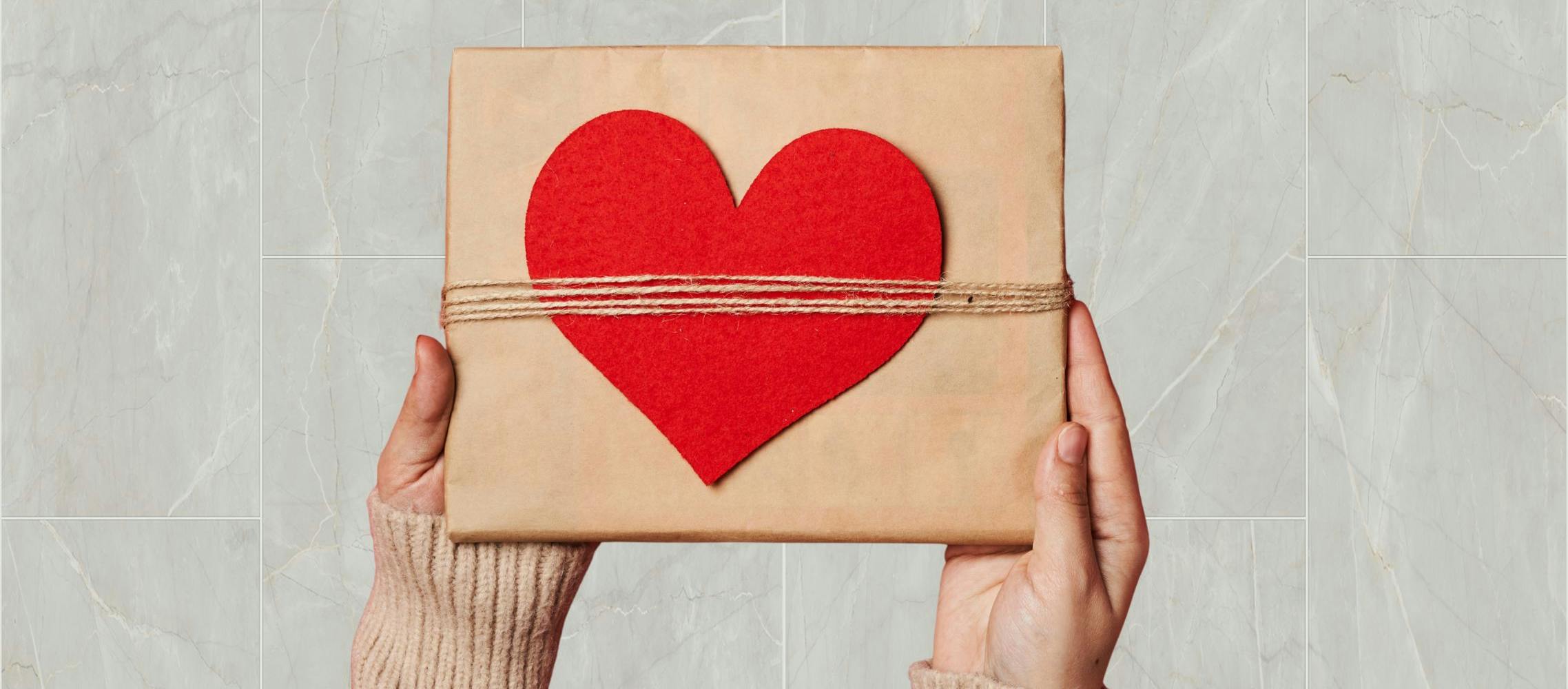 Woman holding up a present wrapped in a heart, symbolizing the gift of love