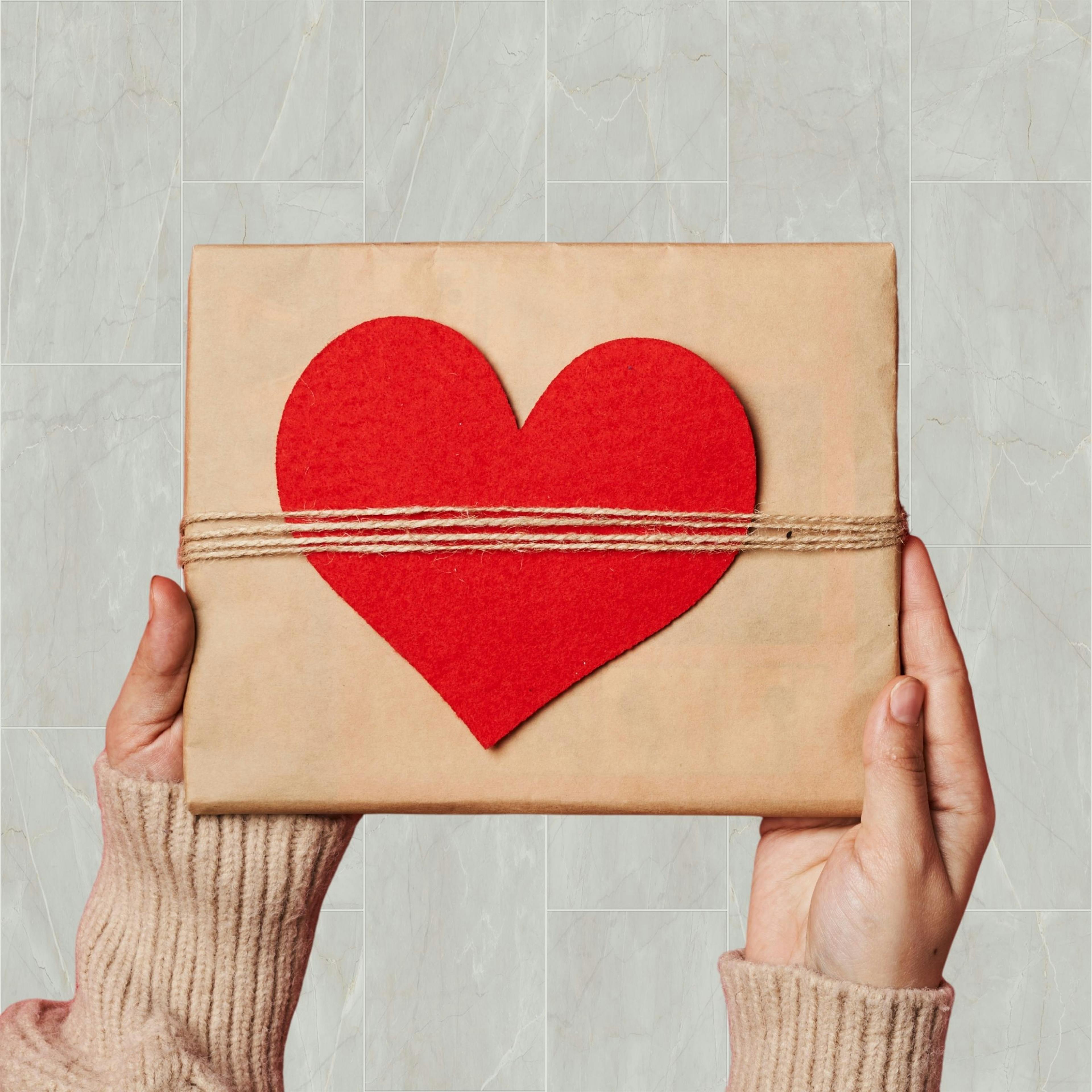 Woman holding up a present wrapped in a heart, symbolizing the gift of love