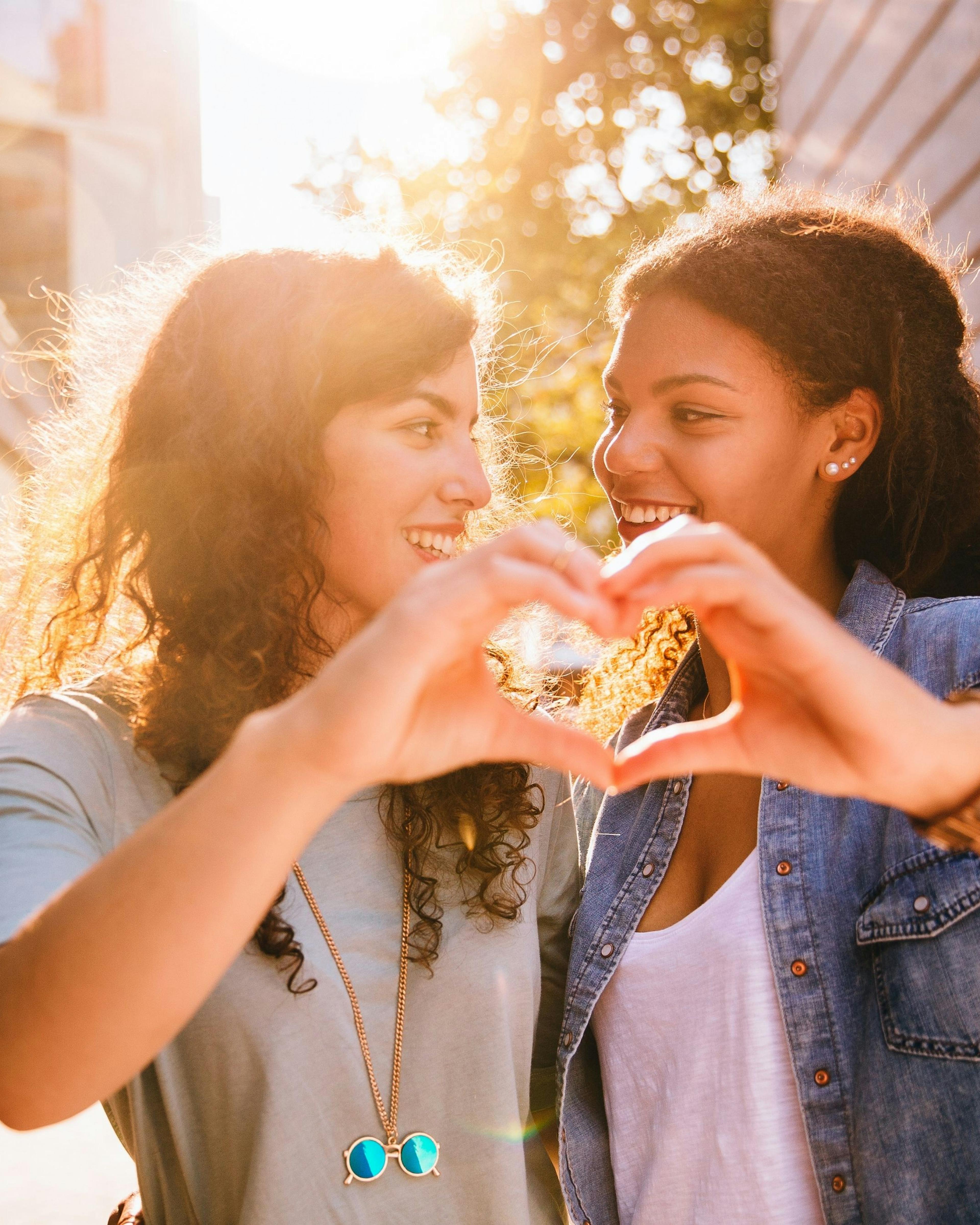 Two best friends laughing together while celebrating a birthday by making a heart with their hands