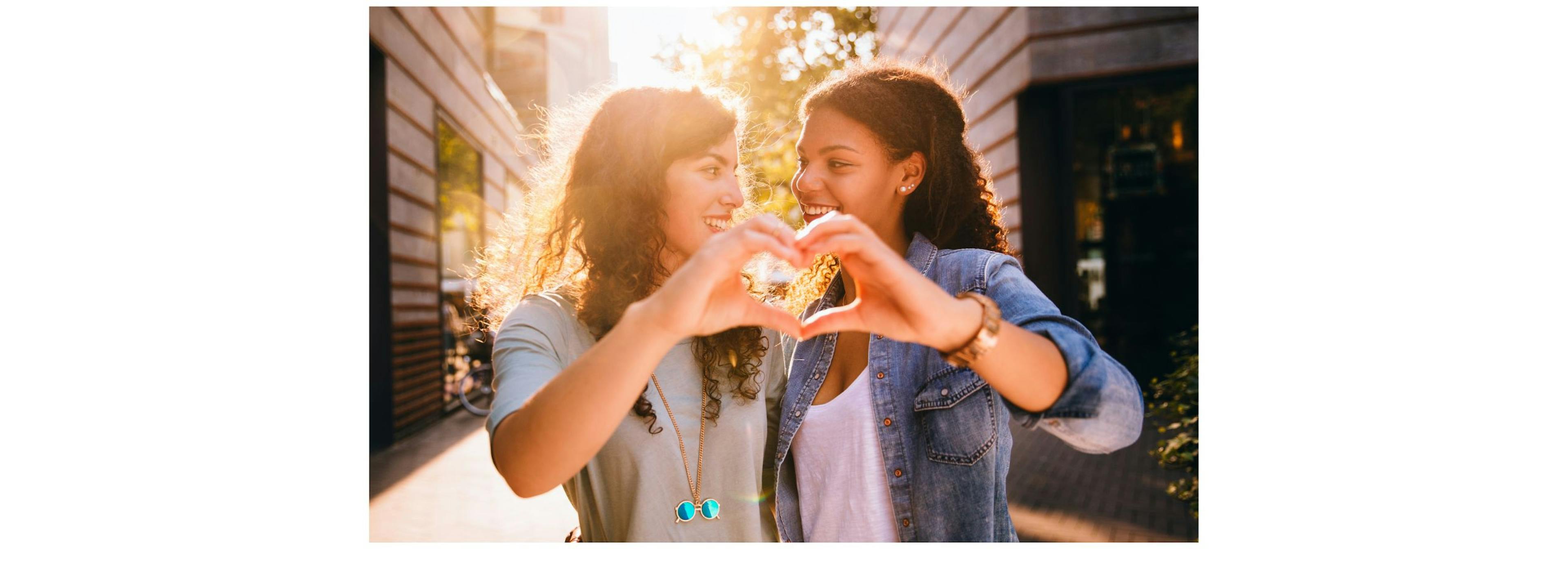 Two best friends laughing together while celebrating a birthday by making a heart with their hands