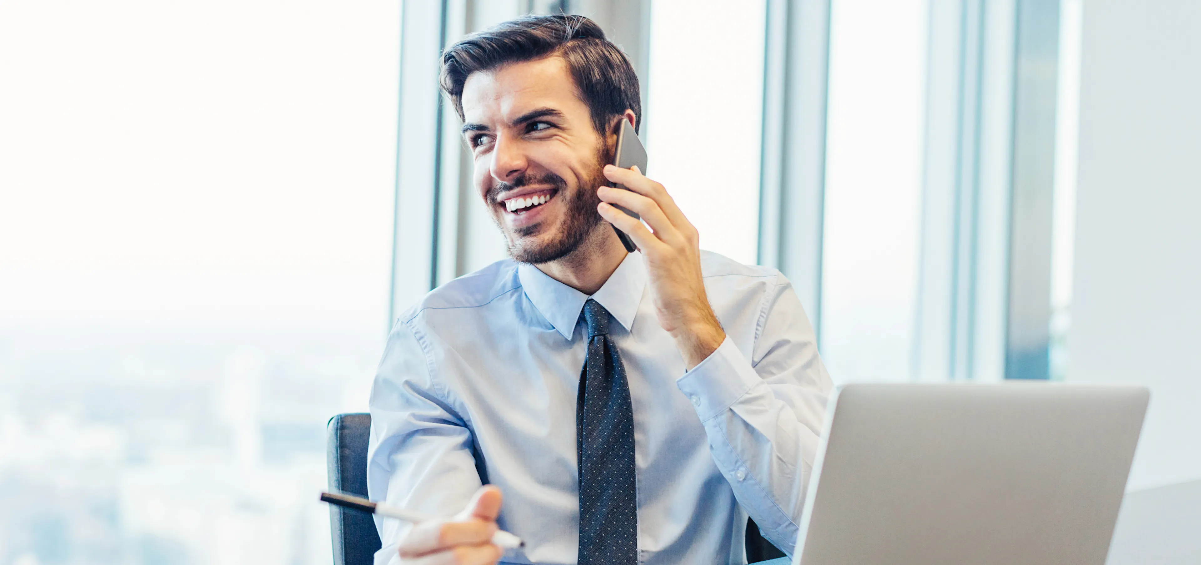 Smiling professional on a phone call at his desk, feeling valued at work, showing how great leaders show appreciation