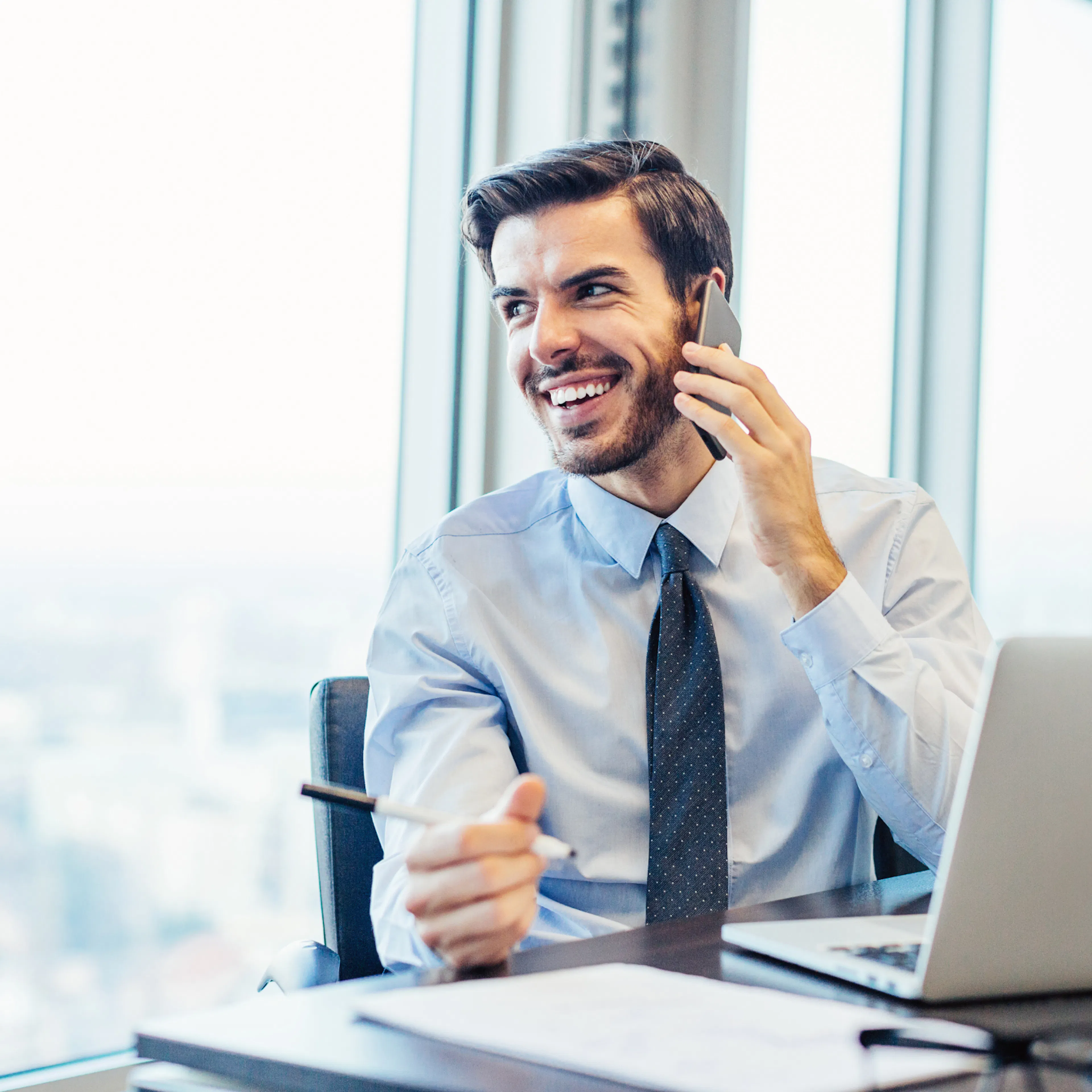 Smiling professional on a phone call at his desk, feeling valued at work, showing how great leaders show appreciation
