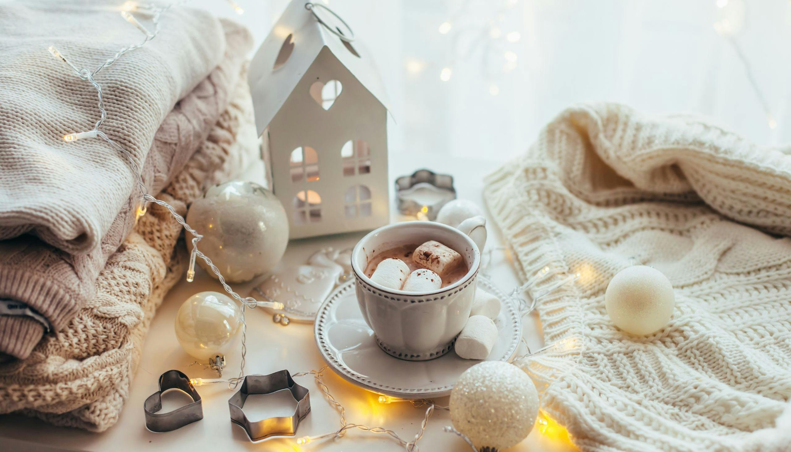 Cozy holiday scene of lights, comfy sweaters and hot cocoa with marshmallows