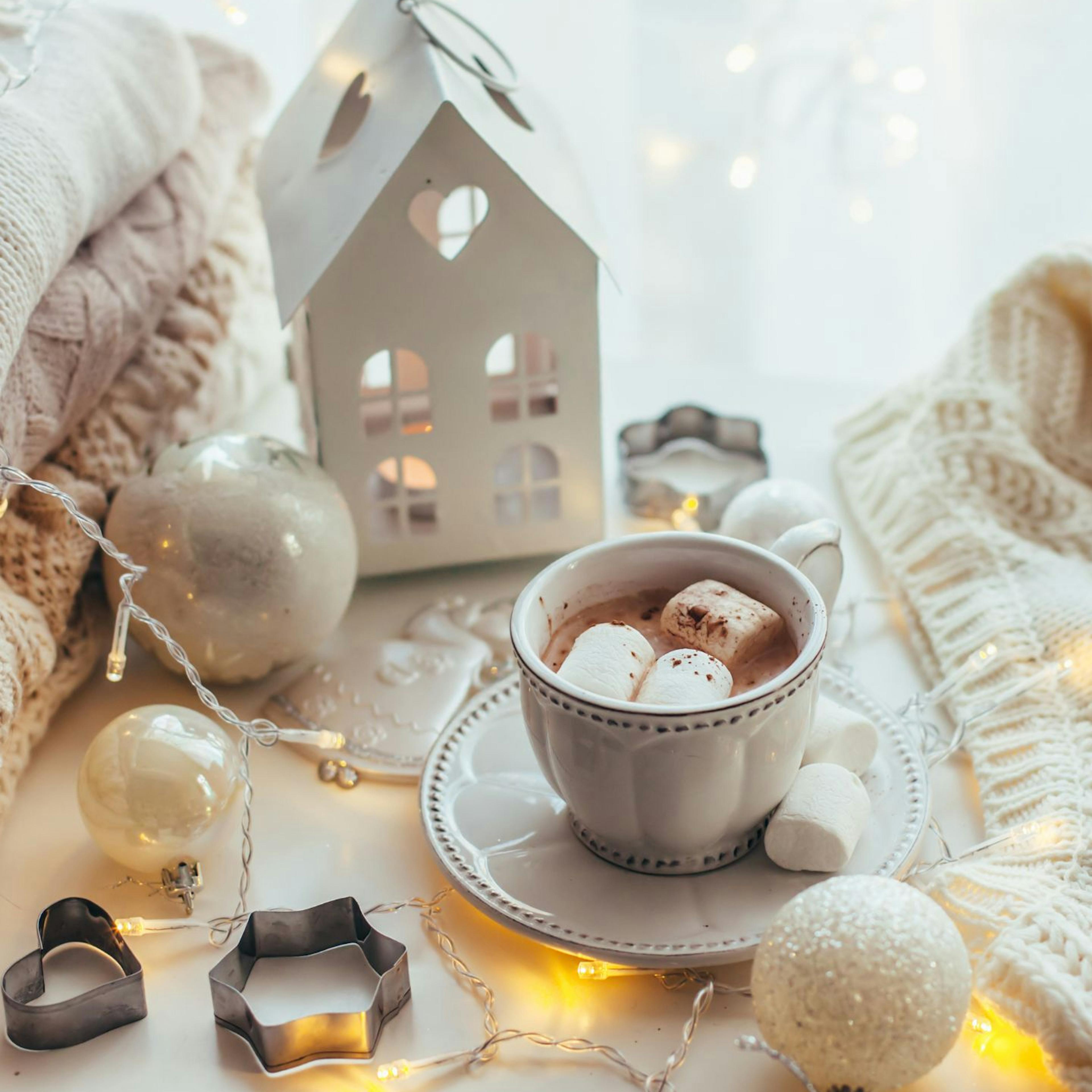 Cozy holiday scene of lights, comfy sweaters and hot cocoa with marshmallows