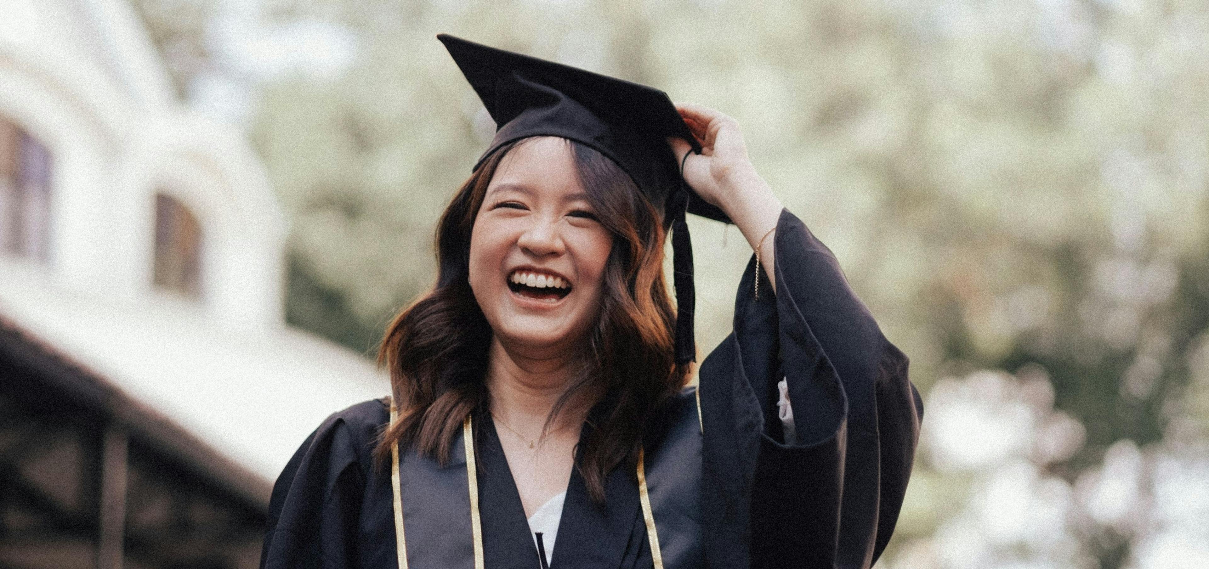 Graduate in cap and gown celebrating with diploma, representing thoughtful graduation gifts including books, travel items, and personal keepsakes
