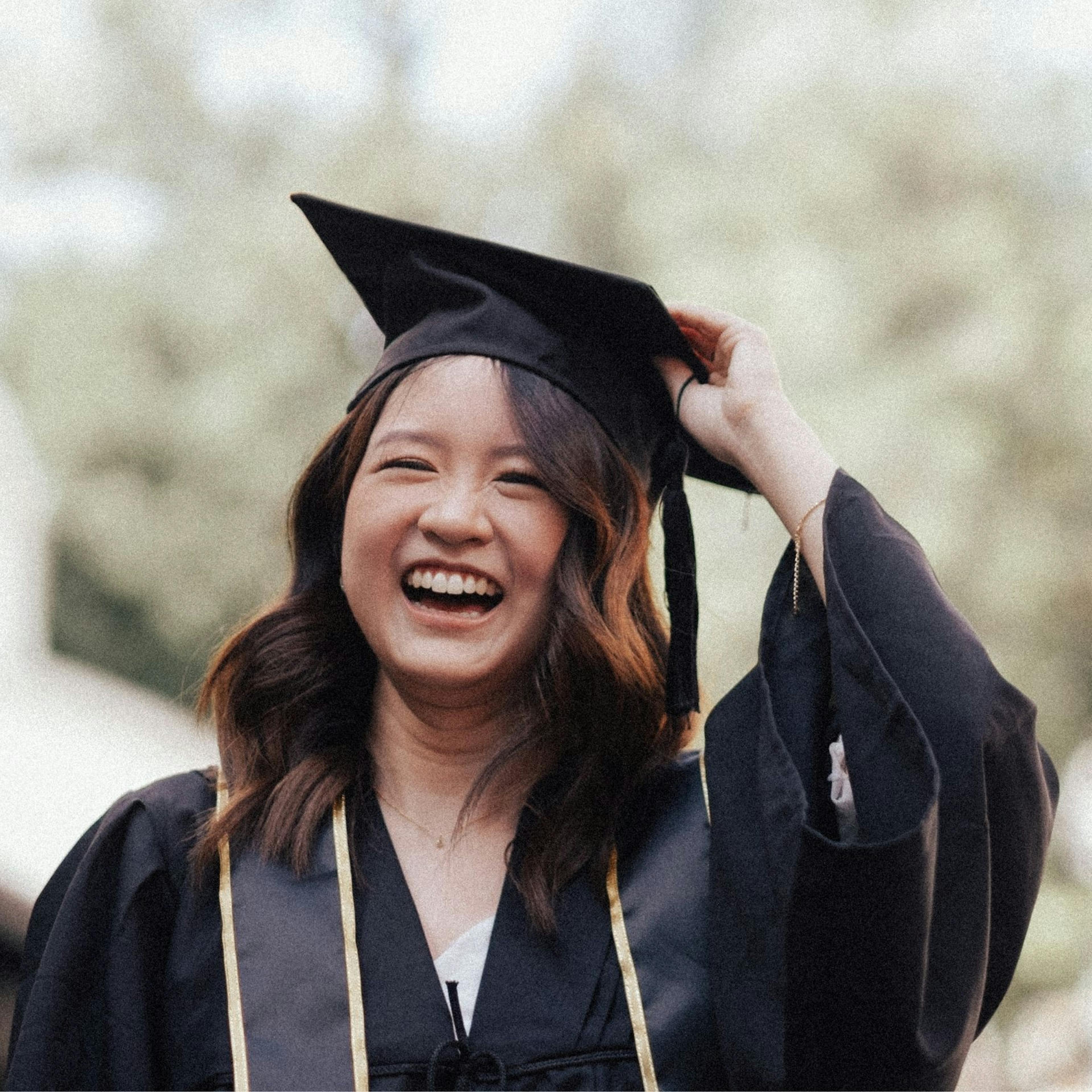 Graduate in cap and gown celebrating with diploma, representing thoughtful graduation gifts including books, travel items, and personal keepsakes