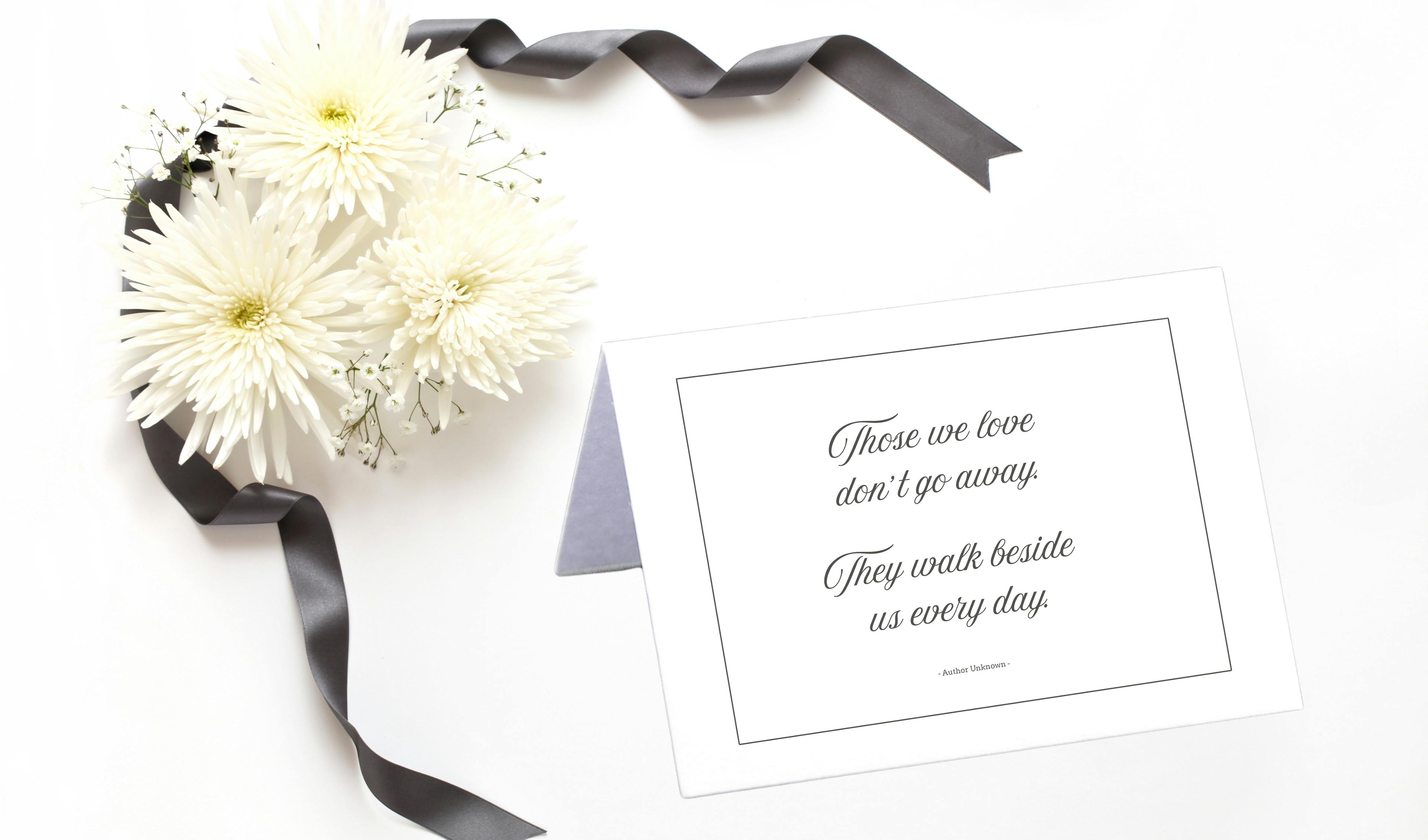 Close-up of fresh flowers and condolence card with a quote that reads "Those we love don't go away. They walk beside us every day. Author Unknown"