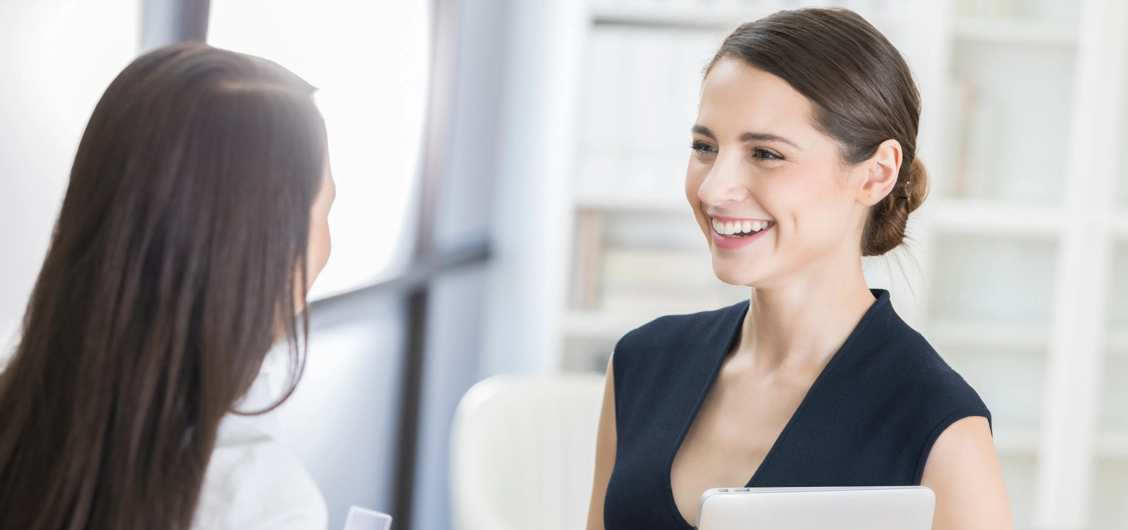 Executive assistant coordinating workplace appreciation with colleague smiling together in modern office