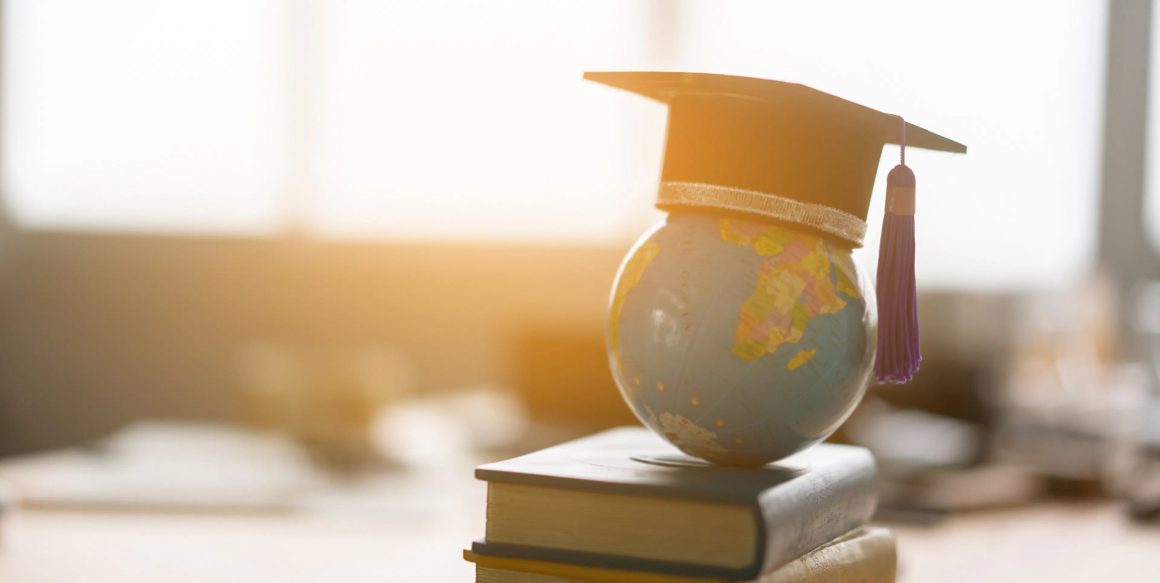 Textbooks and world globe on a desk wtih a graduation cap, signifying the exciting possibilities ahead for a recent graduate