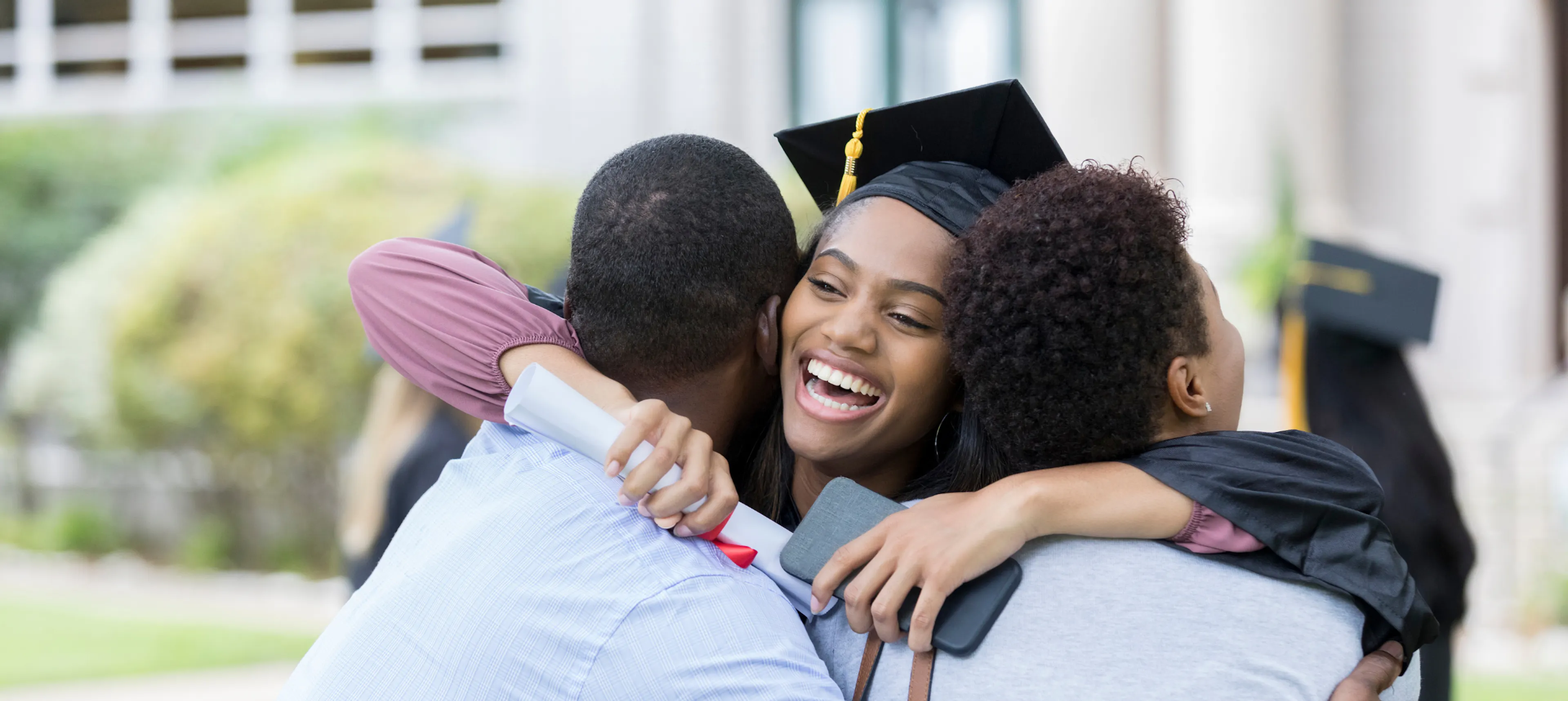 Mother and father hugging their grad as they celebrate graduation day with the gift of love and presence