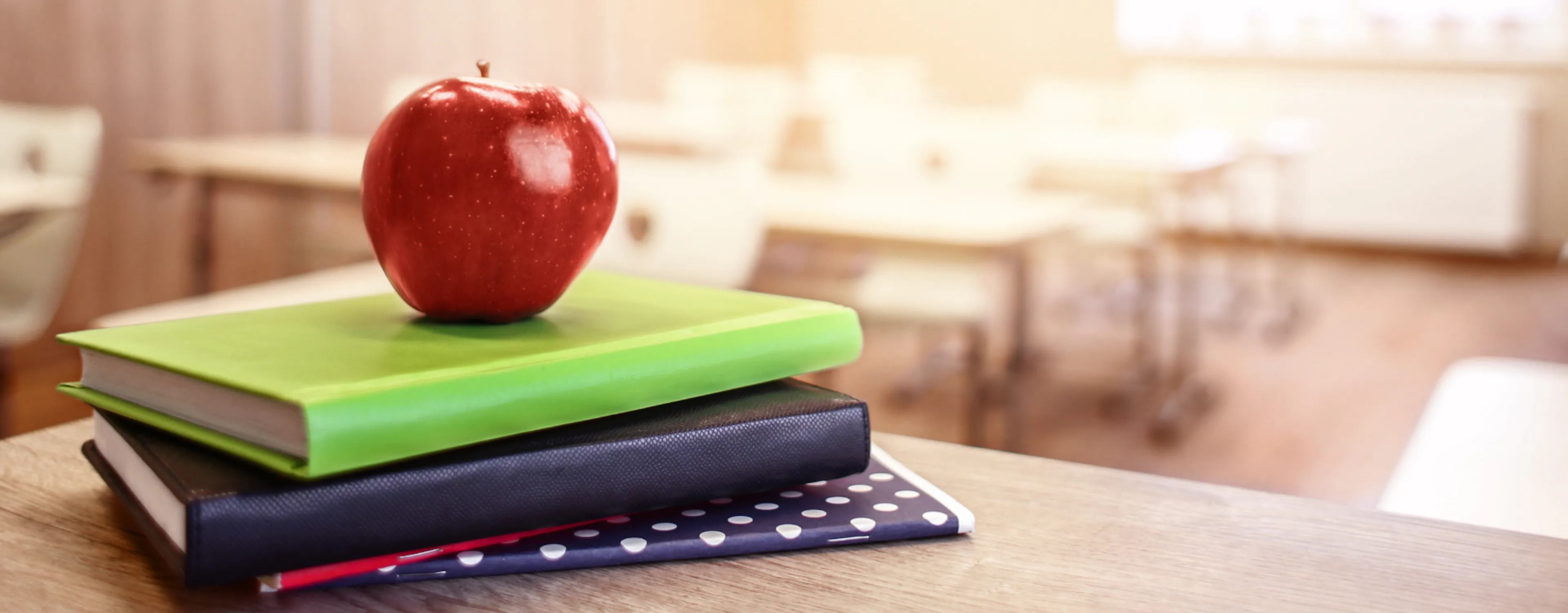 Teacher's books on a desk with an apple on top, representing a teacher gift