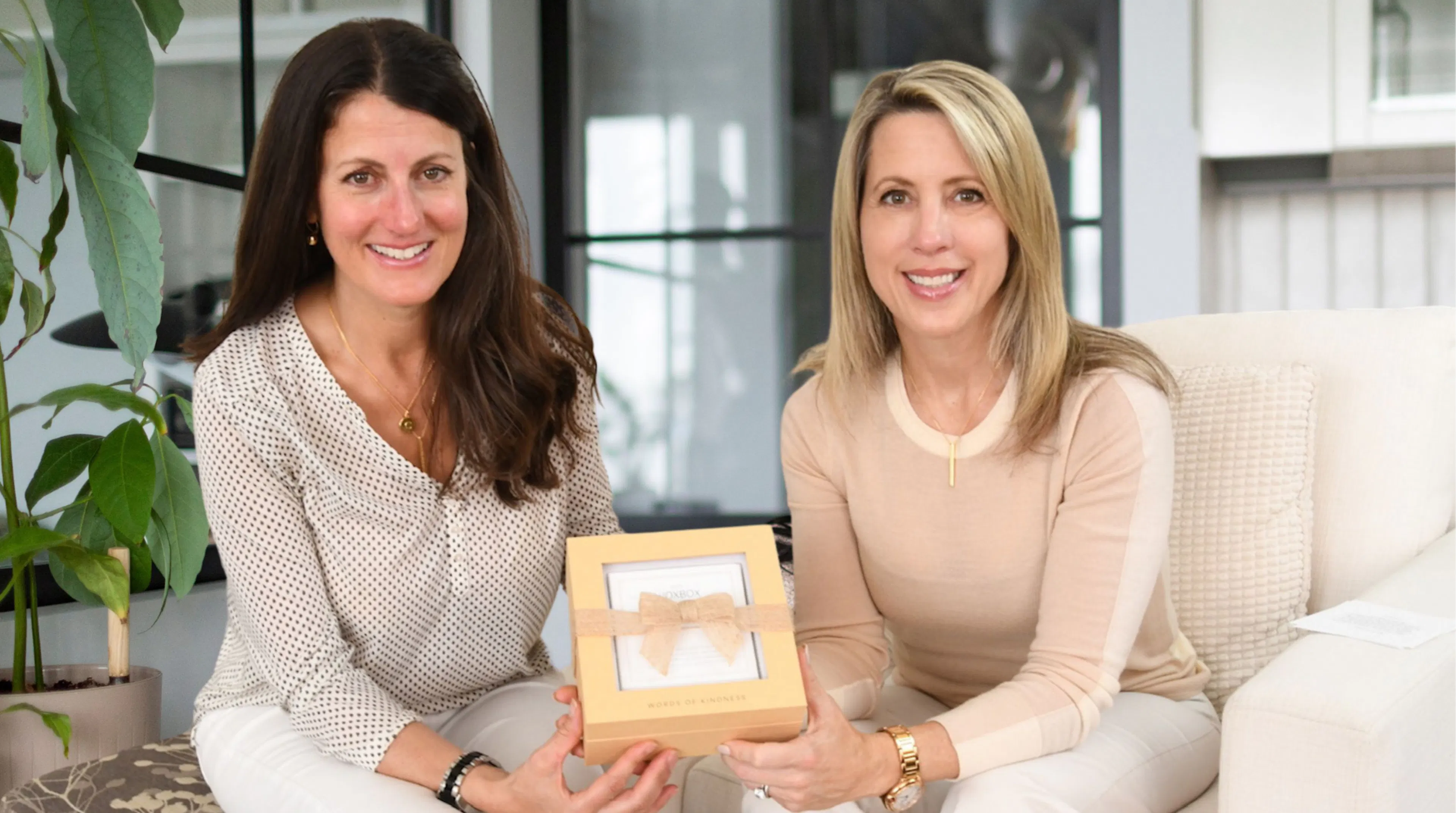 Cindy Iatan and Carey Kirchmair sitting on a sofa smiling while they hold a Woxbox