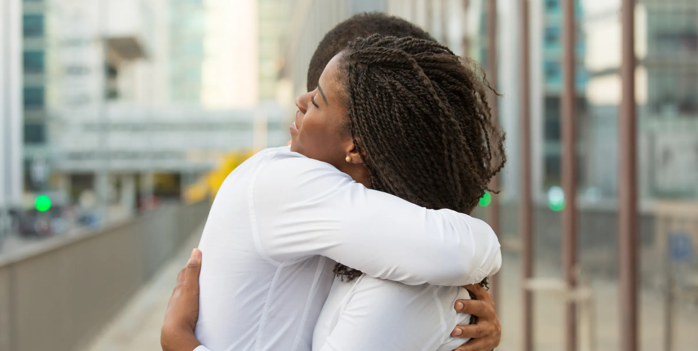 Two sisters hugging while standing outside a building downtown