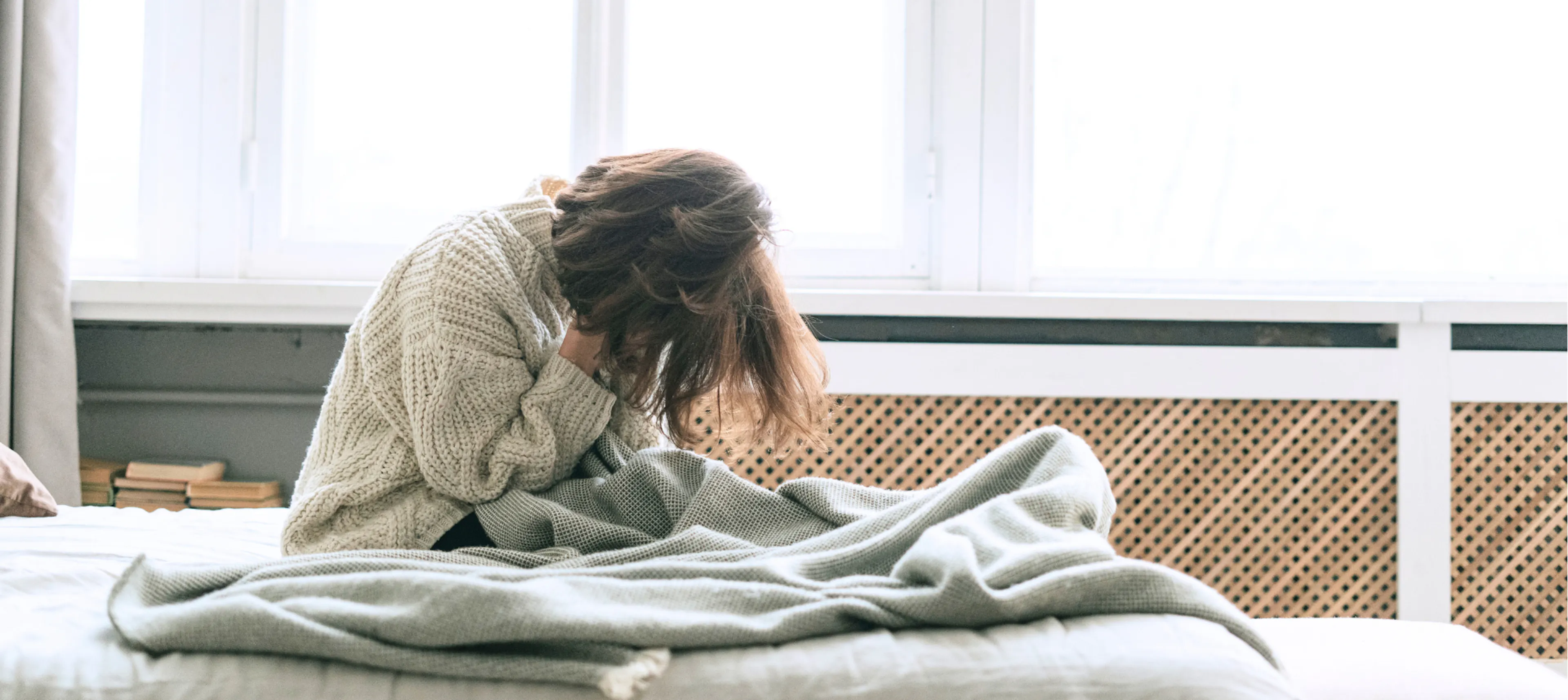 Someone struggling with mental health, sitting on the bed with their head down