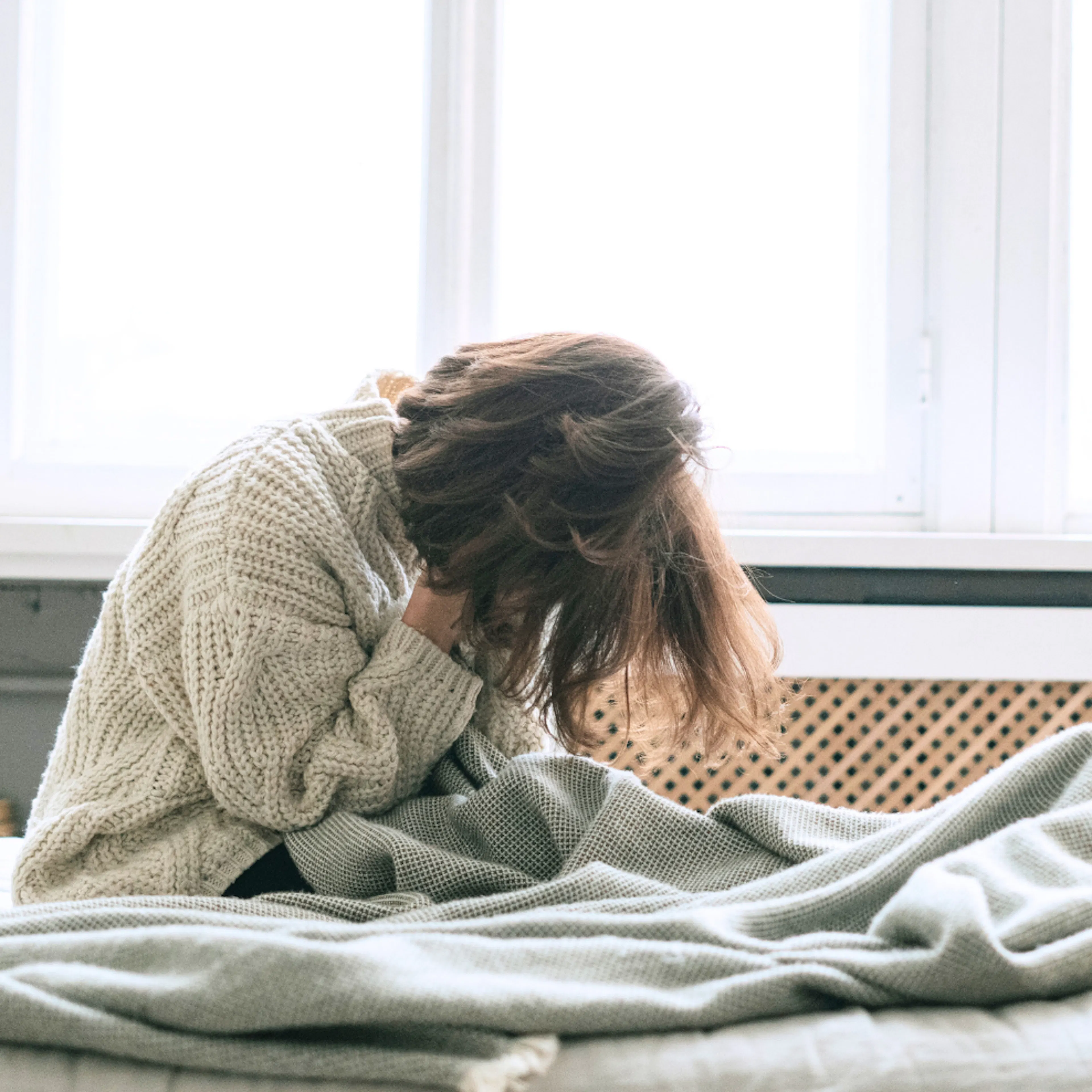 Someone struggling with mental health, sitting on the bed with their head down