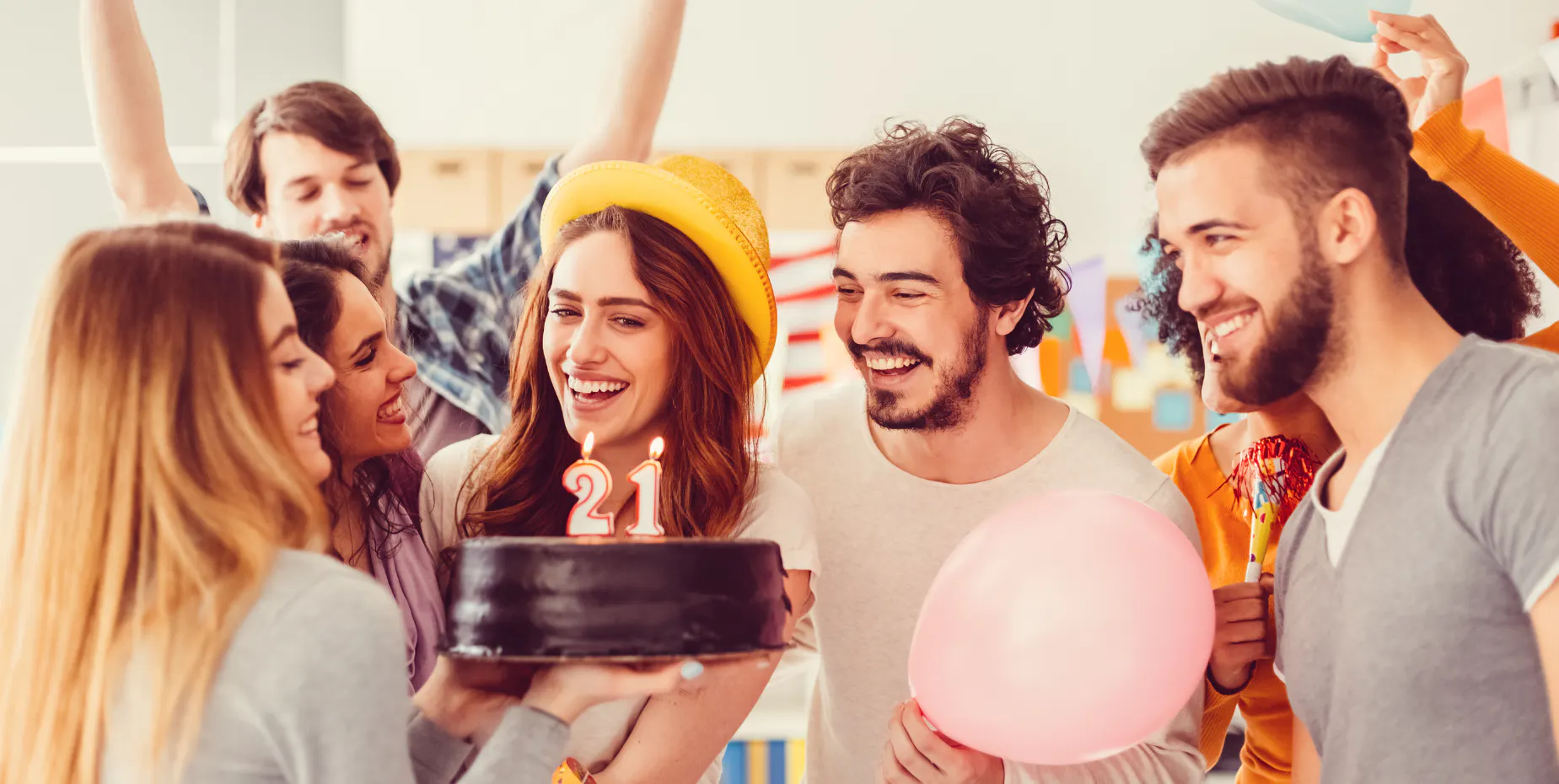 A group of friends laughing together at a birthday celebration while one of them holds a 21st birthday cake