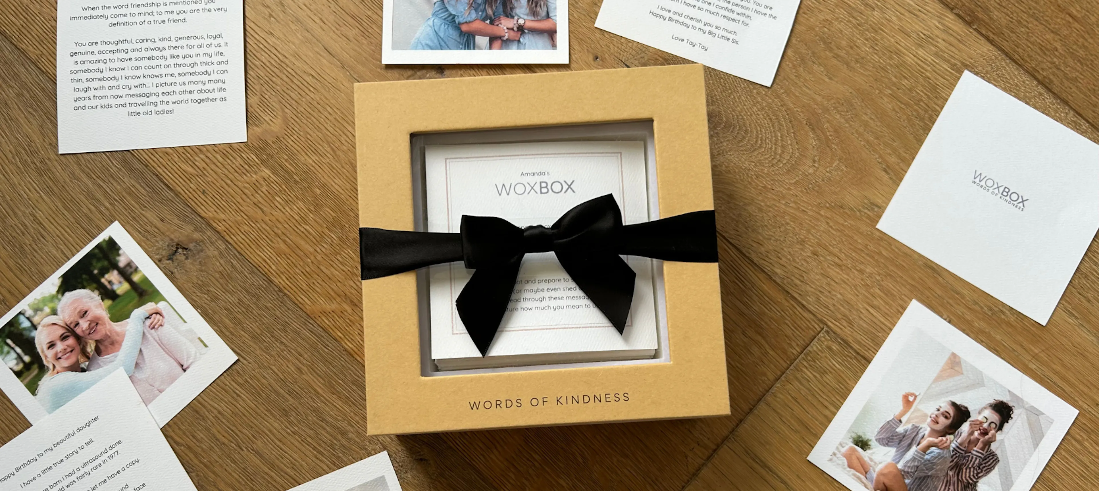 Woxbox keepsake gift box wrapped in a black satin bow, with heartfelt messages and photos around it on the table