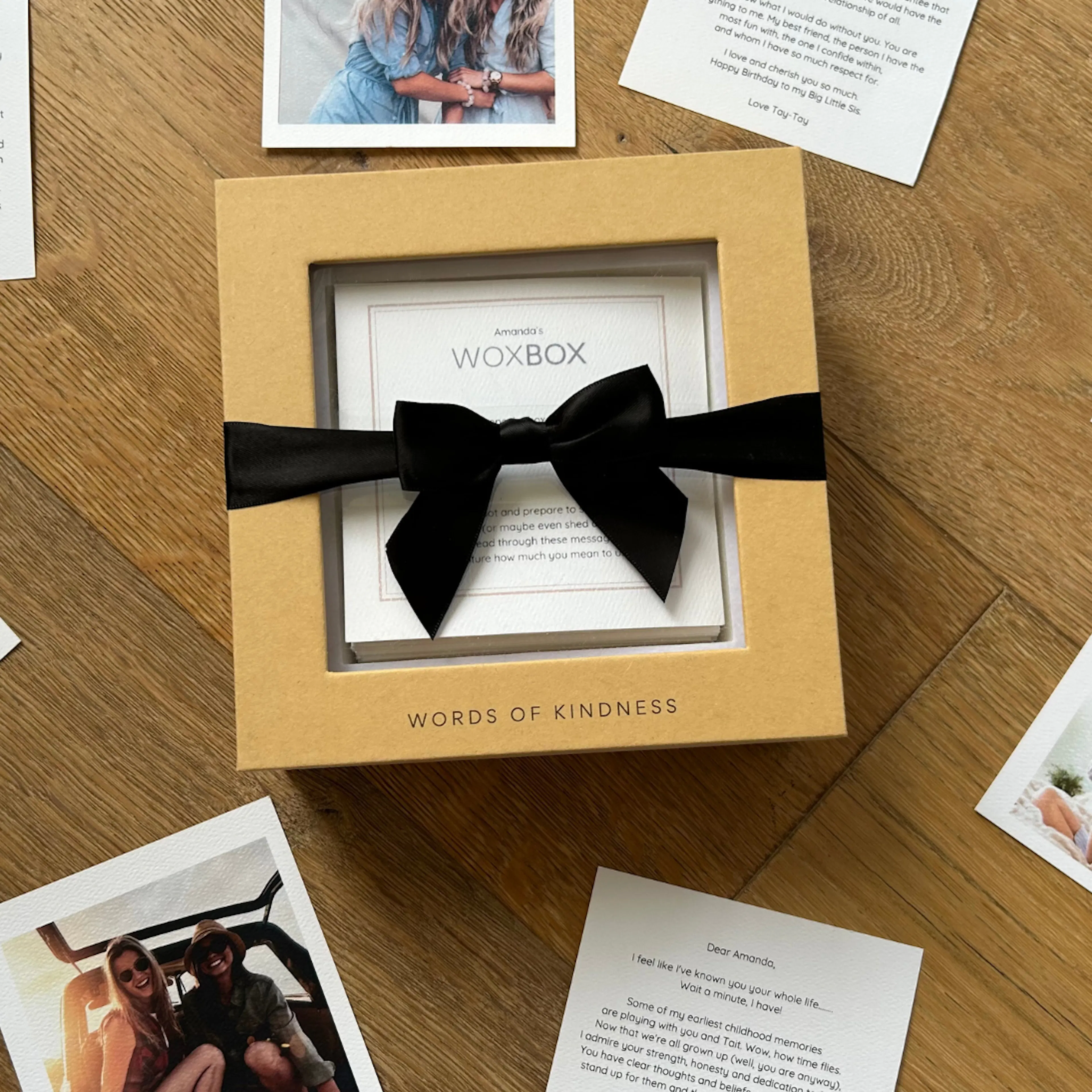Woxbox keepsake gift box wrapped in a black satin bow, with heartfelt messages and photos around it on the table