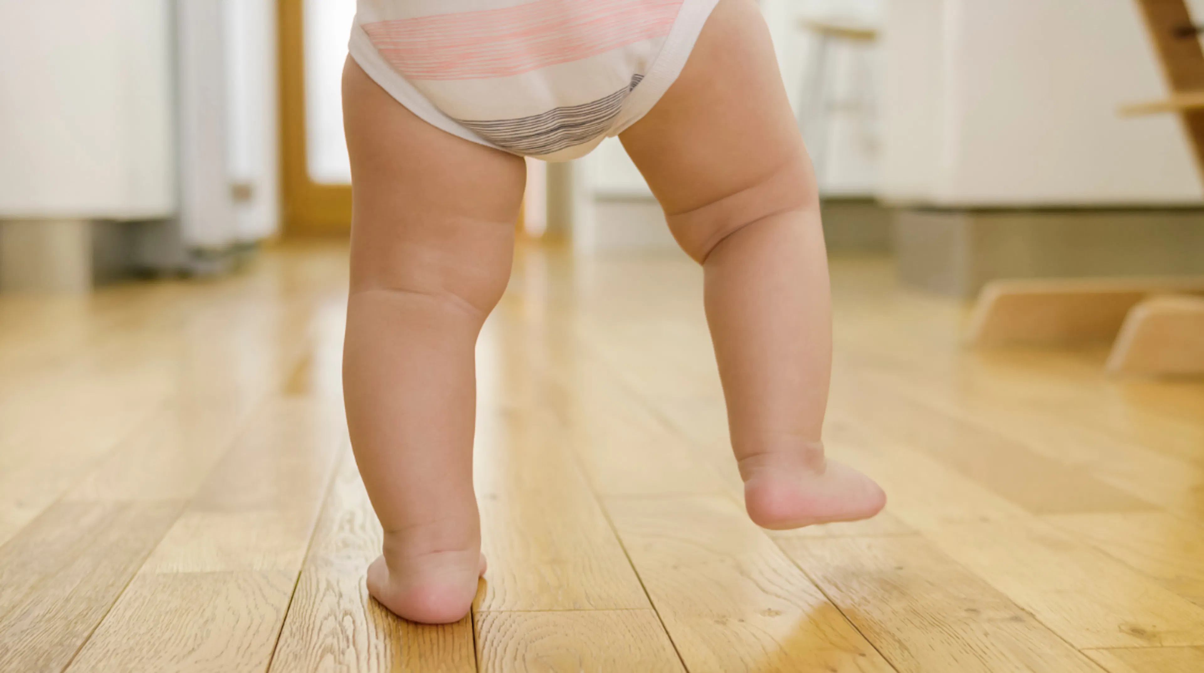 Baby taking first steps, representing the moments and photos to preserve in baby's first year time capsule