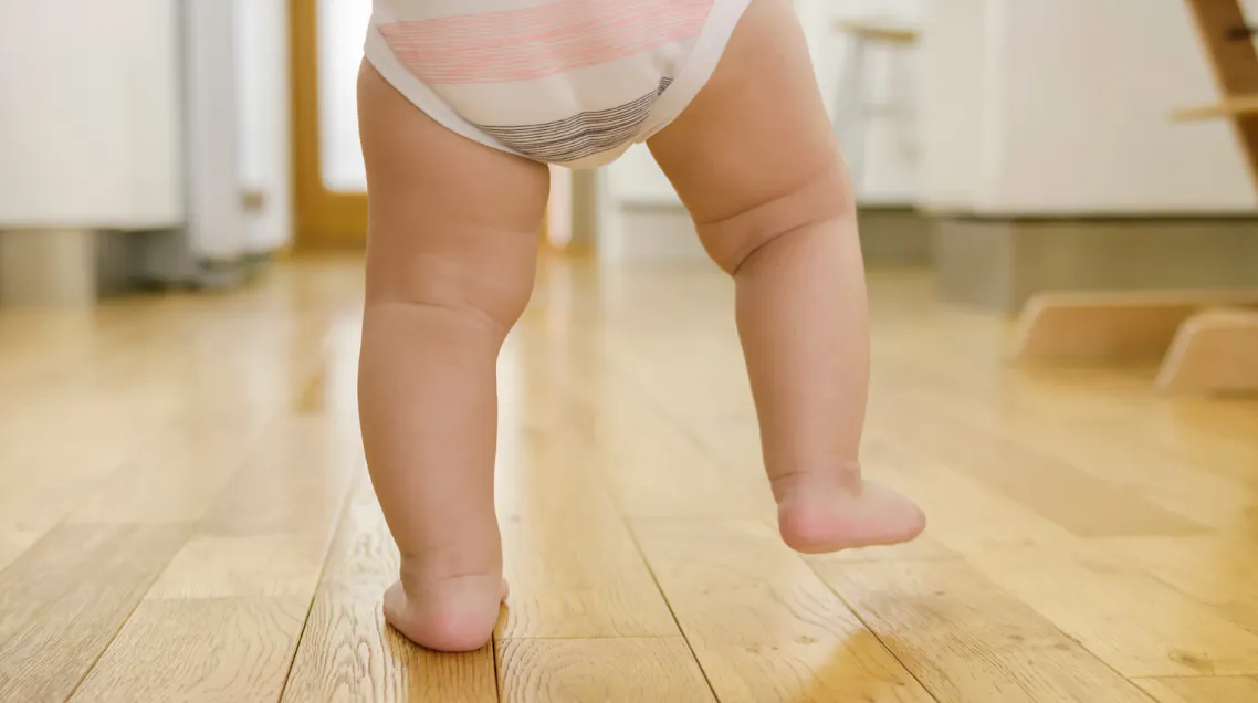 Baby taking first steps, representing the moments and photos to preserve in baby's first year time capsule