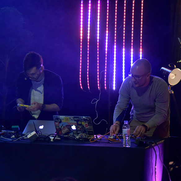 Sam Wray and NERDDISCO on stage at dotJS 2016, LED curtain on display, Sam playing the Game Boy and NERDDISCO using a MIDI controller.