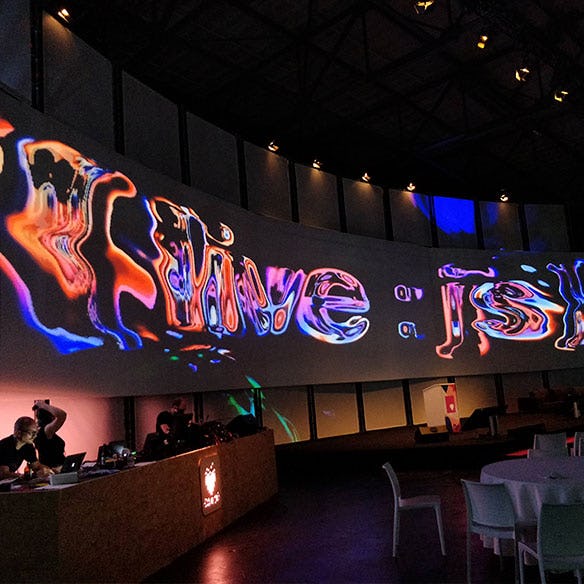 Large colorful projection of the phrase "{ live : js }" at JSConf EU 2018.