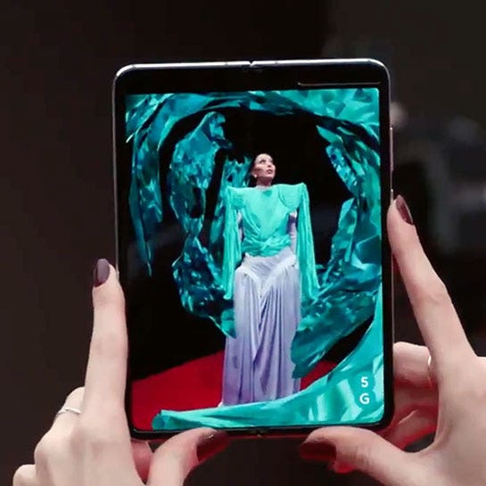 Maya Jama in camera viewport of a Samsung Galaxy Fold with 3D material flying around her in AR