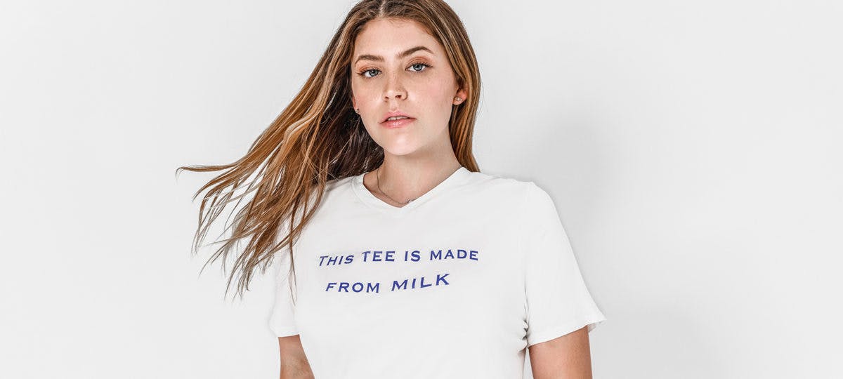 A woman has a white t-shirt on with the text "This tee is made from milk."