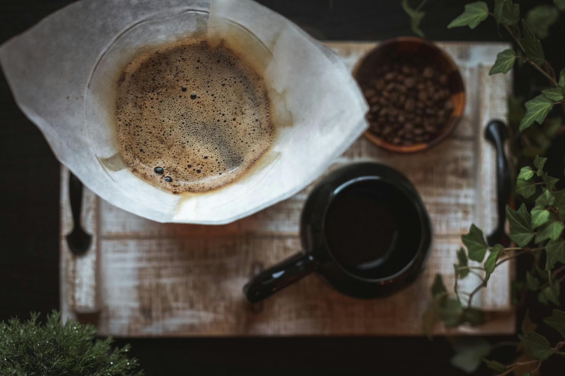 Drip coffee surrounded by a bowl of coffee beans and a black mug.