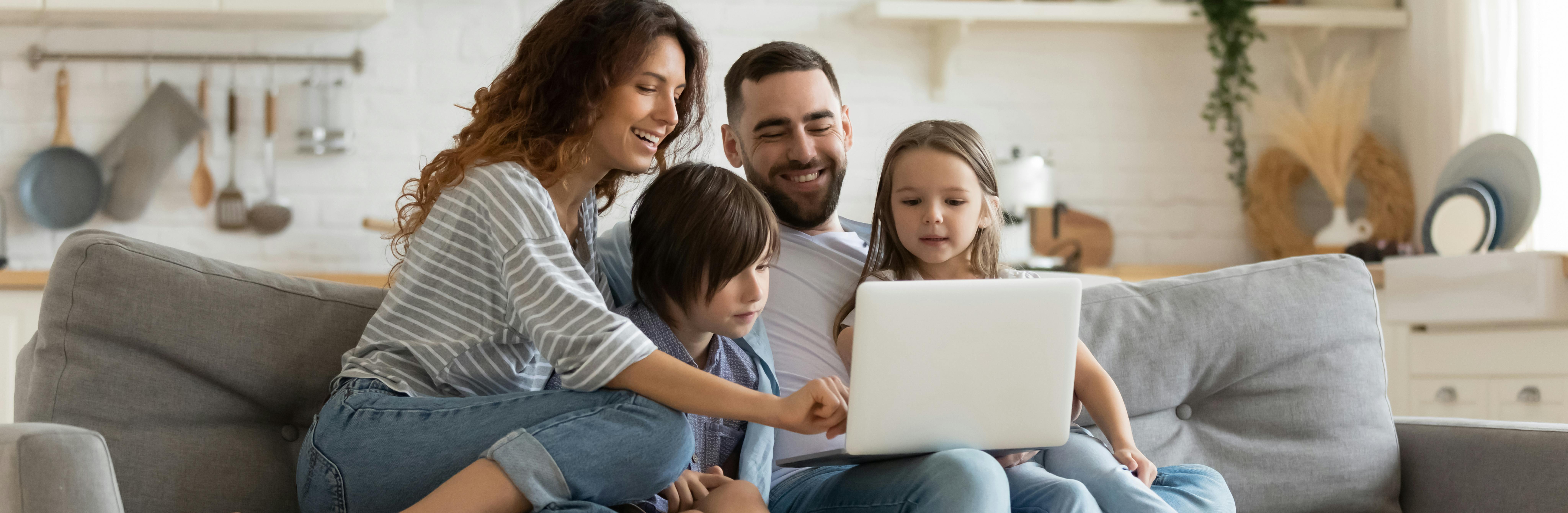 Zwei Eltern und ihr kleiner Junge und ihr kleines Mädchen auf einer Couch schauen auf einen Laptop