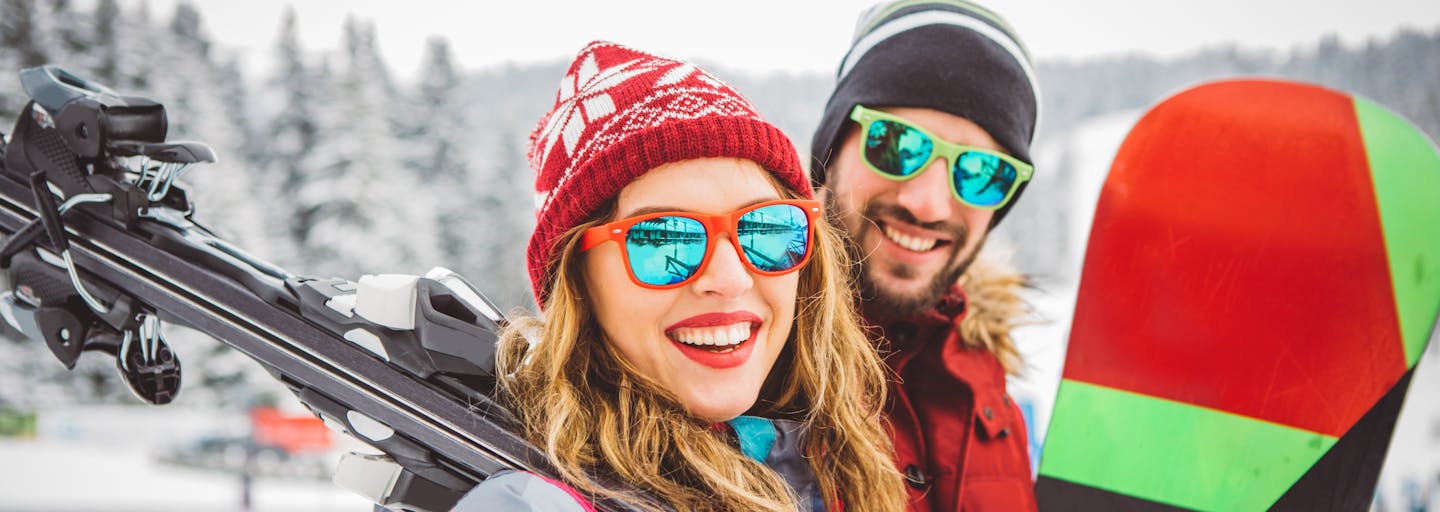 Happy couple carrying their skis and snowboard.