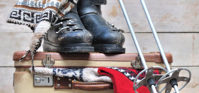 Suitcase with poles boots and beanie resting on top.