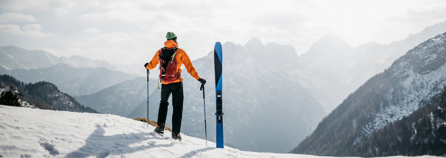 Man standing with skis at the top of a mountain.