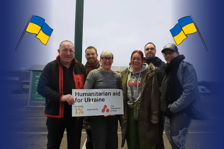 A photo of all six drivers holding a poster with Humanitarian aid for Ukraine with pledge 1% and The Adaptavist Group logos 