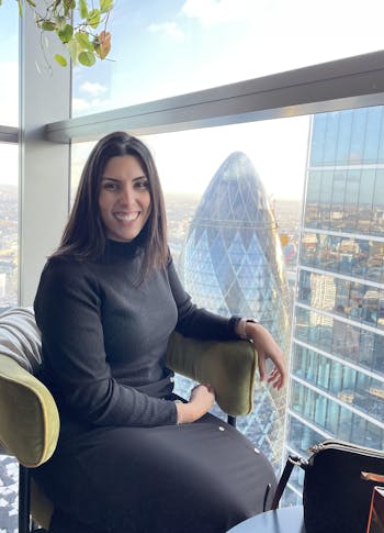 Photo of Rita Gil sitting smiling in front of the Gherkin in London