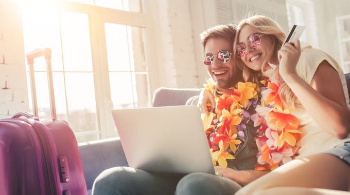 Pärchen bei Urlaubsvorbereitung auf dem Sofa mit Laptop nach Sparpotenzial suchend