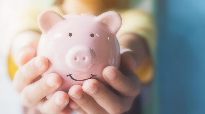 Kinderhände halten lächelndes Sparschwein