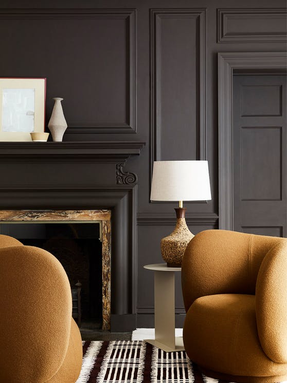 Deep brown paneled living space (Chocolate Colour) with contrasting dark yellow armchairs sat next to a fireplace and lamp.