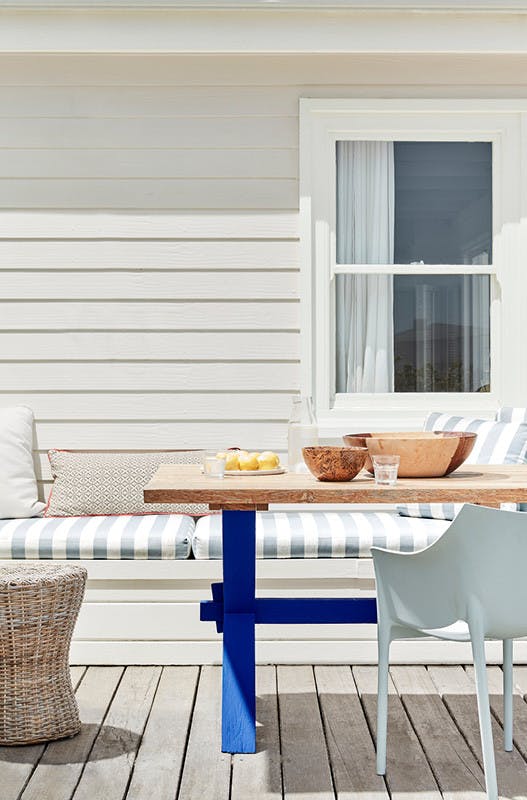 Outdoor dining area with off-white paneled wall (Linen Wash) with a striped cushioned chair and wooden table.