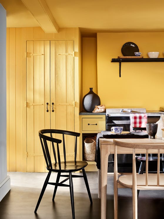 Kitchen painted in bright Giallo yellow on the walls, ceiling and woodwork, with neutral wooden furniture in the foreground.