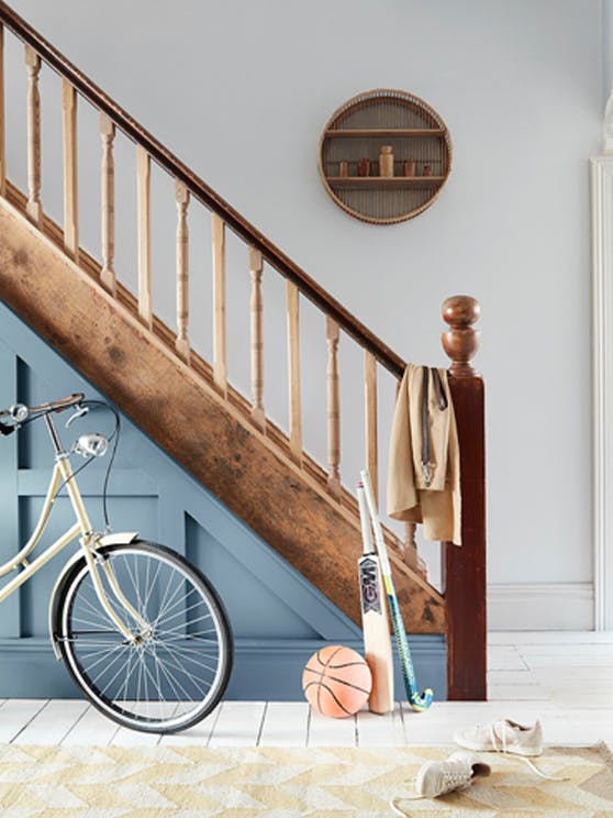 A hallway with white walls and flooring featuring a bike and sports equipment leaning on a blue and brown wooden staircase.