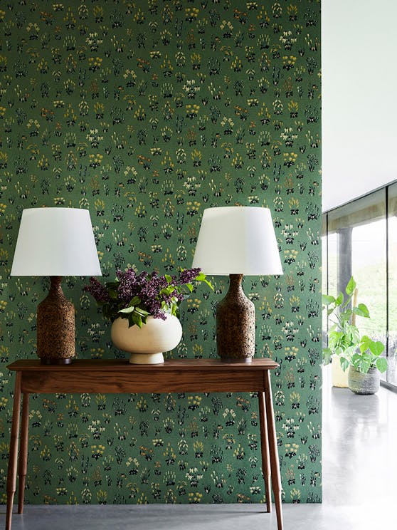 Hallway with green small floral wallpaper 'Millefleur - Garden' and a wooden sidetable with two lamps and a vase of flowers.