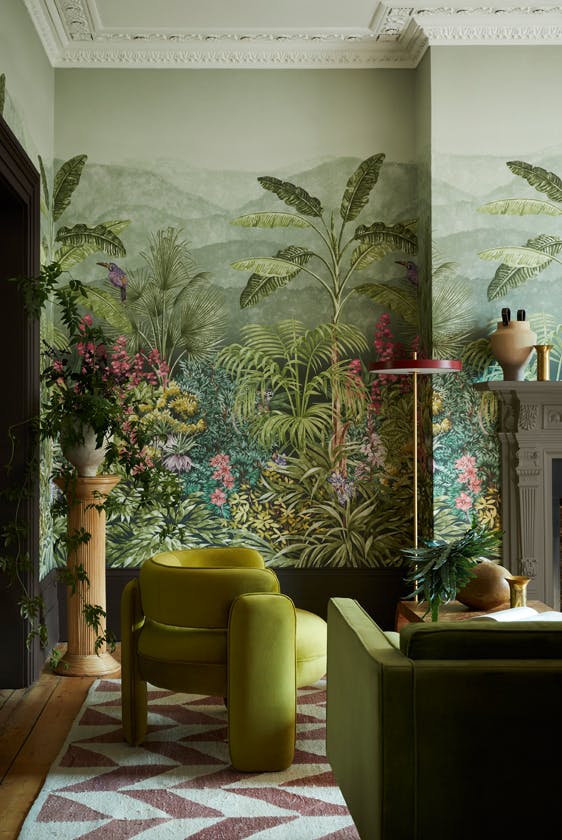 Living space featuring green tropical mural wallpaper (Capricorn - Boringdon) with a green armchair and sofa next to a fireplace.