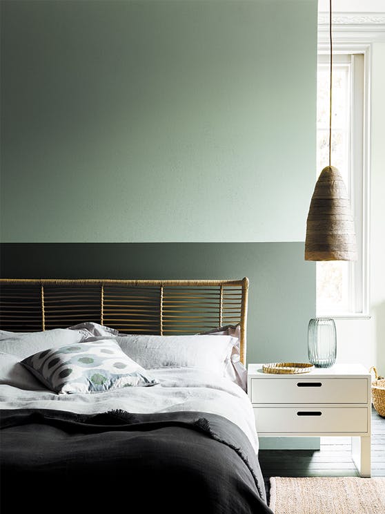 Bedroom with a wall painted half and half in two shades of green, behind a bed and white side table.