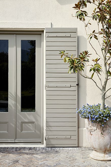 Back door with stone grey (Serpentine) shutters and off-white (Slaked Lime - Deep) walls with a big potted on the right.