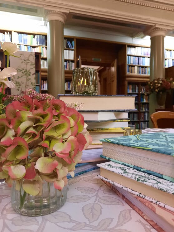 Close-up of table centerpieces including a clear vase with flowers and books covered with National Trust Papers III patterns.
